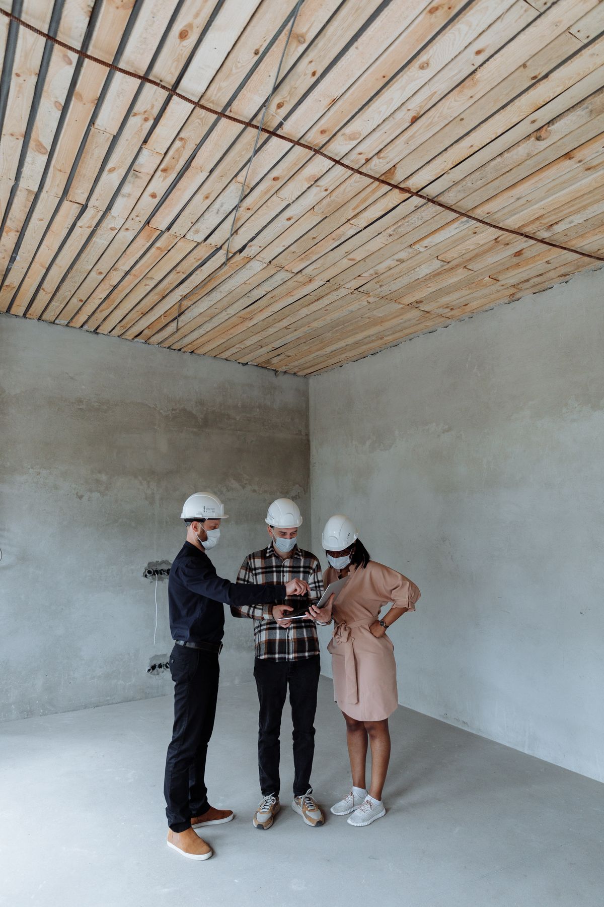 Professionals in hard hats reviewing a laptop at an unfinished building