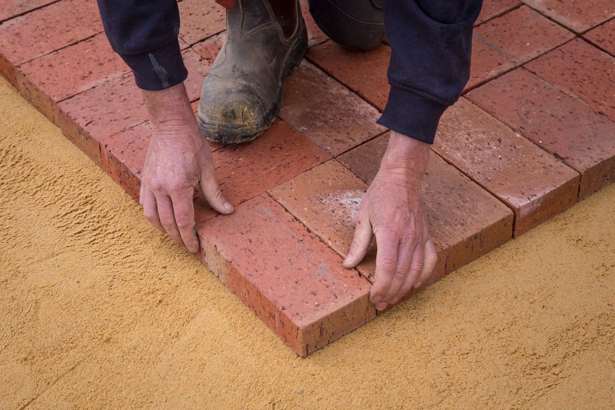 Hands aligning paving bricks on a prepared base